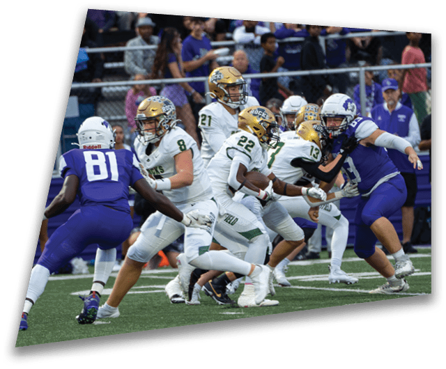 Four people in dark football uniforms and helmets stand in a row on a field, appearing focused and ready for action. Description generated by AI