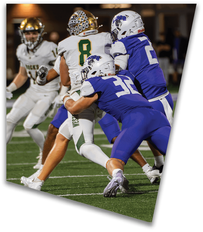 A person wearing a dark football uniform and helmet with “American Canyon" on the jersey is kneeling on one knee on a field at night. Description generated by AI