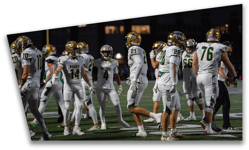 People wearing black American Canyon football uniforms and helmets are standing on a football field at night. Description generated by AI