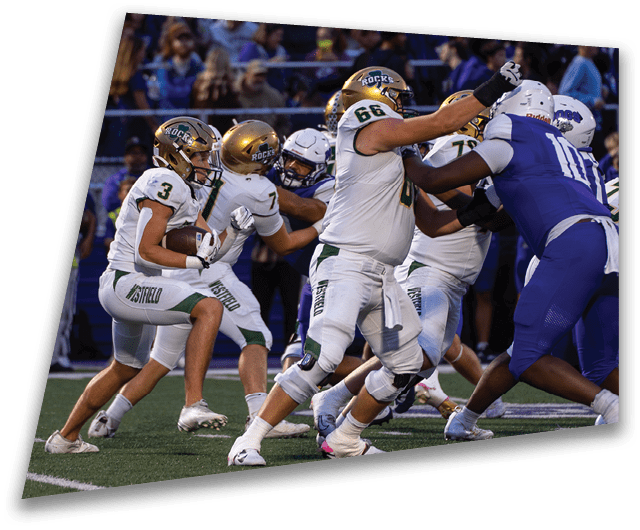 Four people in dark football uniforms and helmets stand in a row on a field, appearing focused and ready for action. Description generated by AI