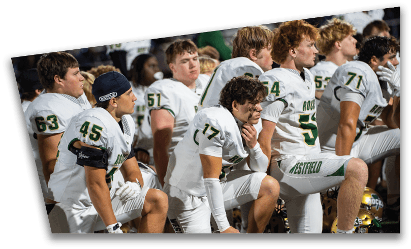 People wearing black American Canyon football uniforms and helmets are standing on a football field at night. Description generated by AI
