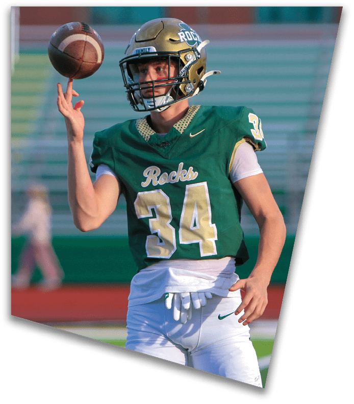 A person wearing a dark football uniform and helmet with “American Canyon" on the jersey is kneeling on one knee on a field at night. Description generated by AI