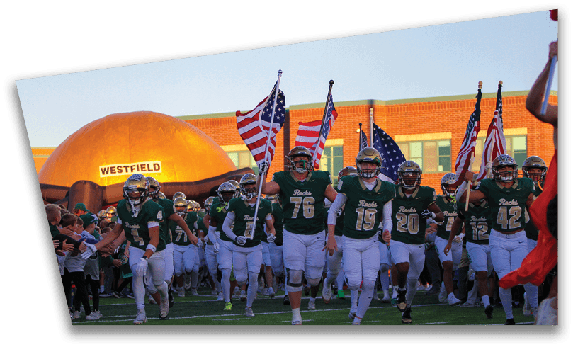 People wearing black American Canyon football uniforms and helmets are standing on a football field at night. Description generated by AI