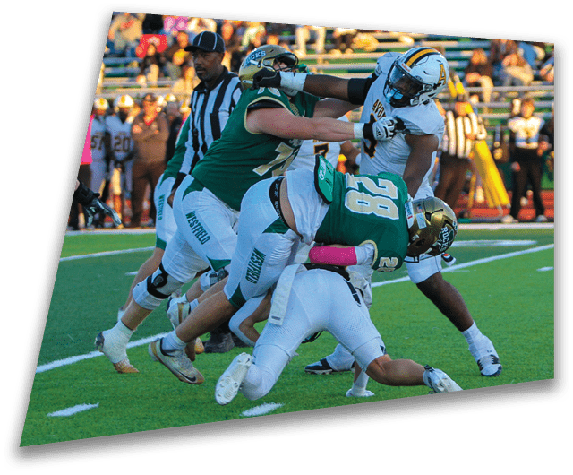 Four people in dark football uniforms and helmets stand in a row on a field, appearing focused and ready for action. Description generated by AI
