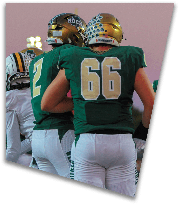 A person wearing a dark football uniform and helmet with “American Canyon" on the jersey is kneeling on one knee on a field at night. Description generated by AI