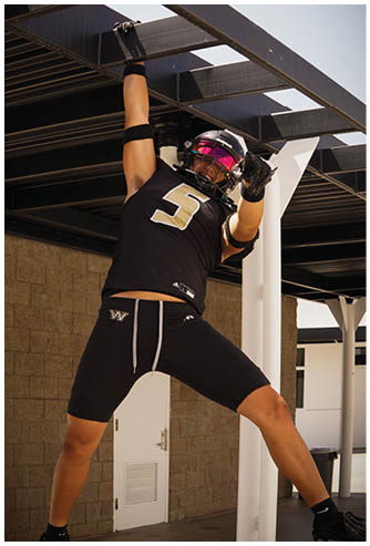 An arm wearing a black wristband is gripping a metal bar of a black outdoor structure against a clear sky. Description generated by AI