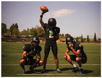 A person wearing a helmet is raising one arm holding a football against a clear sky with a few clouds. Description generated by AI
