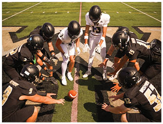 A person wearing a black helmet and white sports jersey is on a football field with empty bleachers in the background displaying the words Westview and Home of the Wolves. Description generated by AI
