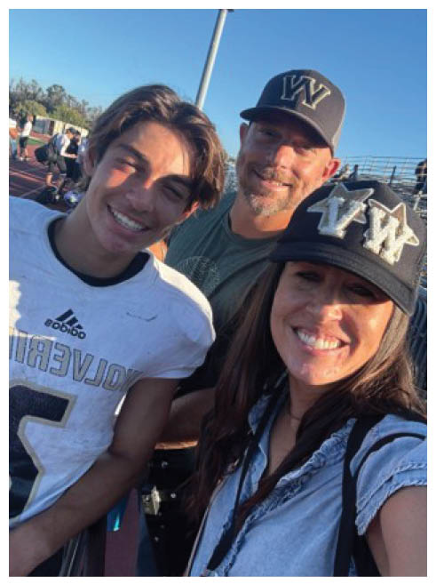 Three smiling people, one wearing a sports jersey and two wearing caps, pose closely together outdoors on a sunny day. Description generated by AI
