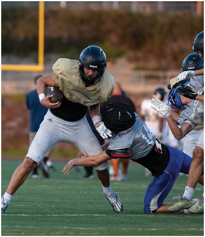 People wearing sports uniforms are engaged in a dynamic moment of a football game on a grassy field. Description generated by AI