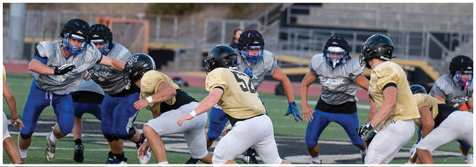 A person wearing black athletic shoes is running on a green artificial turf field with white yard lines. Description generated by AI