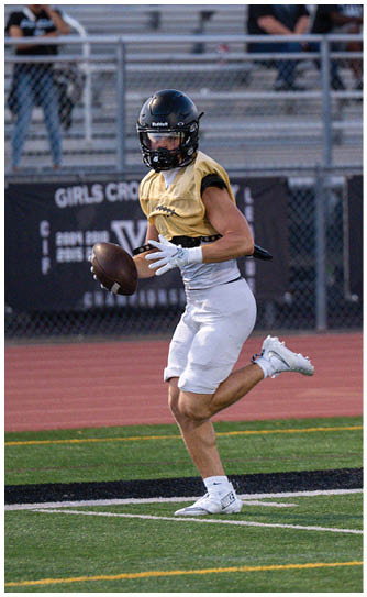 People in sports uniforms are running on a football field near an orange marker with the number 10. Description generated by AI