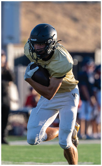 An adult wearing a yellow shirt and white football pants is running on a field while holding a football tightly. Description generated by AI