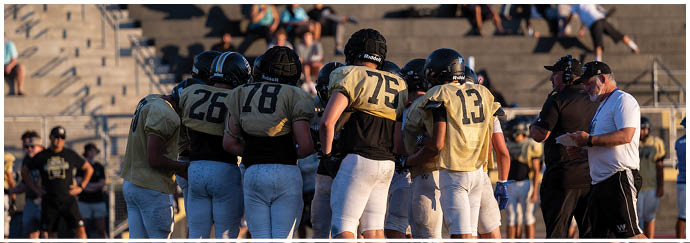 A group of people wearing sports uniforms and cleats are standing together on a grassy field, likely preparing for or participating in a team sport. Description generated by AI