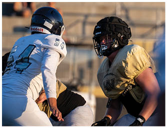People wearing football uniforms and gloves are engaged in a game on a grassy field. Description generated by AI