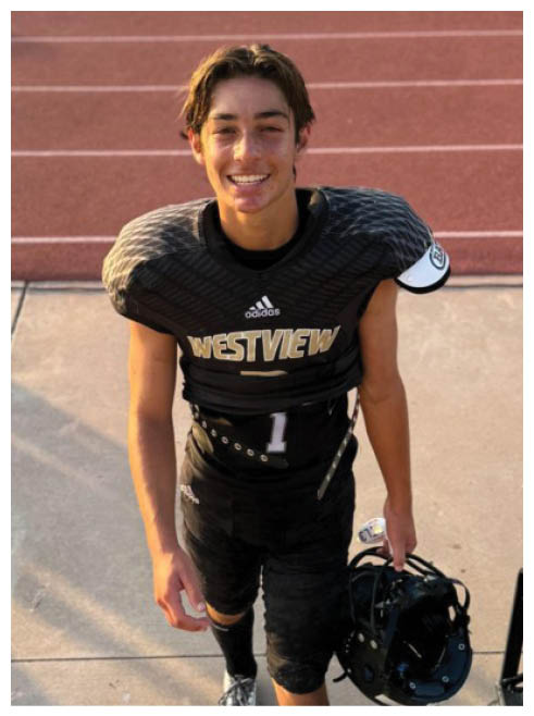 A person wearing a black football uniform with “WESTVIEW" on the chest and holding a helmet is standing on a track and smiling. Description generated by AI