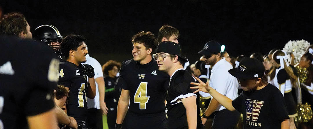 Four people wearing black sports jerseys with “VISTA" on them stand closely together in front of a large crowd, with one person raising an arm in celebration. Description generated by AI