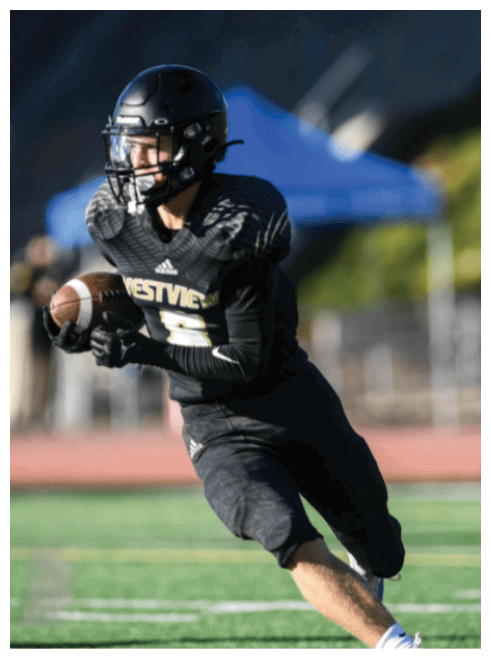 Two people in football uniforms are jumping and reaching for the ball on a field with spectators in the background. Description generated by AI