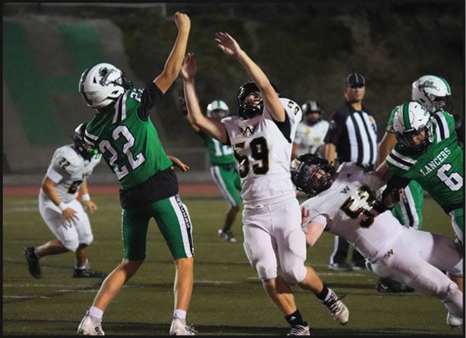 Two people in football uniforms are engaged in a play on a field, with one wearing green and white and the other in white and black. Description generated by AI