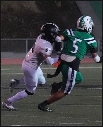 A person in football gear is running on a field while three people stand in the background near the sideline at night. Description generated by AI