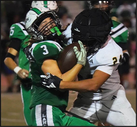 Two people in football uniforms are engaged in a tackle during a game, with one wearing green pants labeled “Lancers" and the other in white pants. Description generated by AI