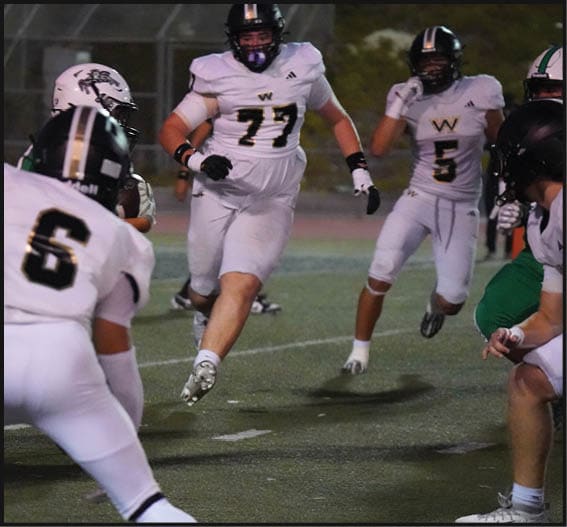 People in white and green football uniforms are actively playing on a field during a game. Description generated by AI