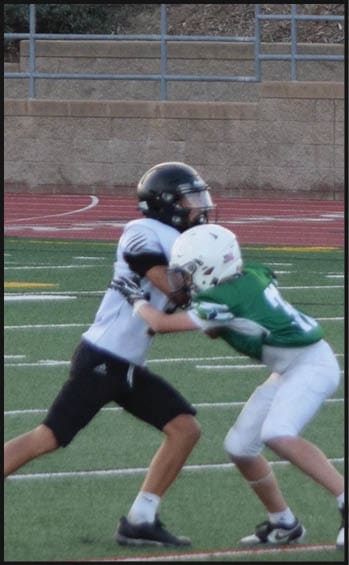 Two people in football gear are engaged in a tackle on a sports field while another person in football gear stands nearby. Description generated by AI