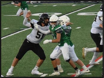 Several people wearing football helmets and uniforms are actively engaged in a play on a grassy field marked with yard lines. Description generated by AI