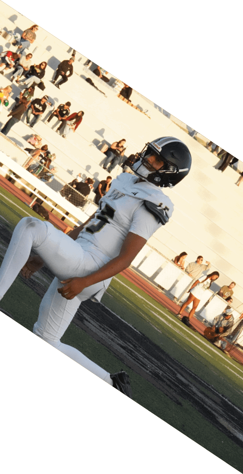 A person in a white football uniform and helmet is kneeling on a field with spectators in the background. Description generated by AI