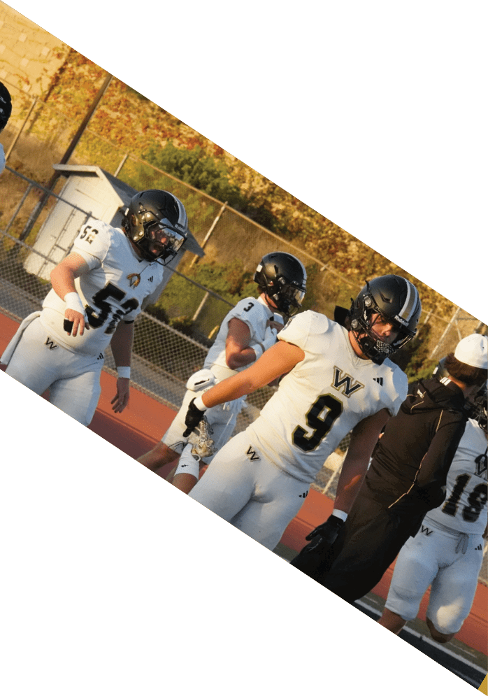People wearing white football uniforms with black helmets are standing on a sports field near a coach dressed in black. Description generated by AI