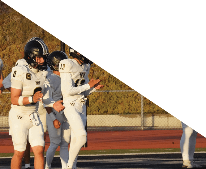 Three people in white football uniforms stand on a field with a track and fence in the background. Description generated by AI