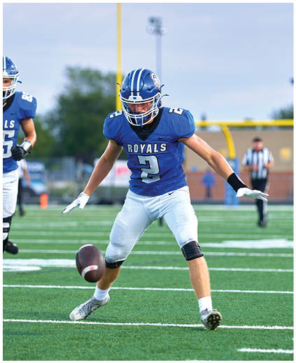A football player in a blue and white uniform is kicking a football. Description generated by AI