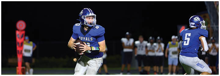 A football player in a blue jersey is running with a football. Description generated by AI
