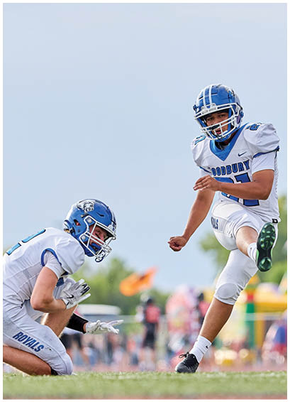 A man in a blue and white uniform is kicking a football. Description generated by AI