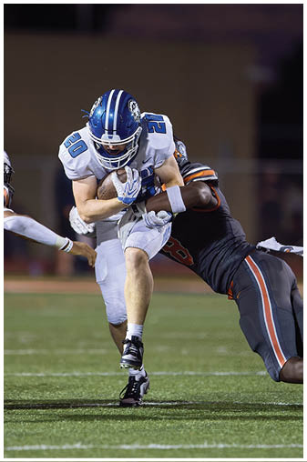 A football player in a blue and white uniform is tackled to the ground. Description generated by AI