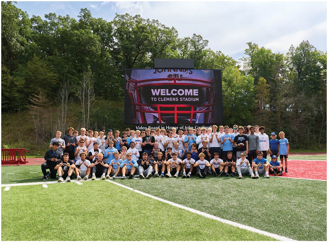 A group of people standing on a football field in front of a large screen. Description generated by AI