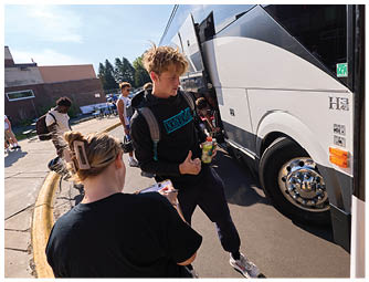 A man wearing a black shirt and blue jeans is standing next to a bus. Description generated by AI