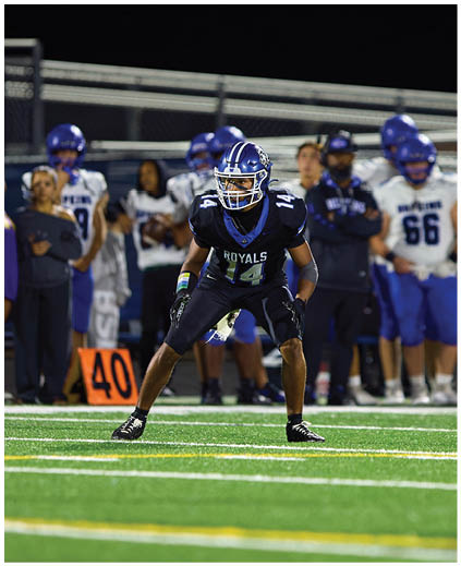 A football player in a blue and white uniform is kicking a football. Description generated by AI