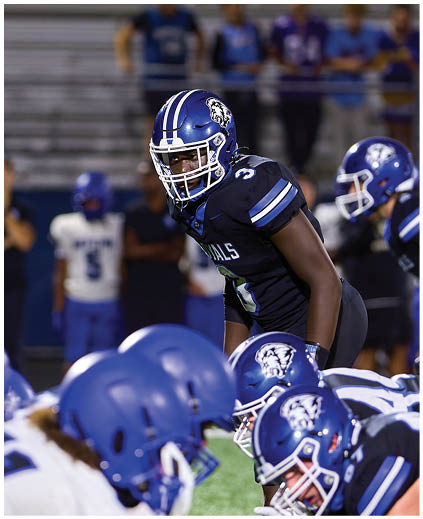 A football player in a blue and white uniform is kicking a football. Description generated by AI