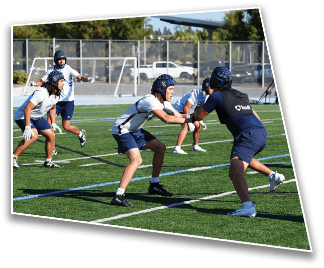 People wearing athletic clothing and cleats are standing and moving on a grass field marked with white and blue lines. Description generated by AI
