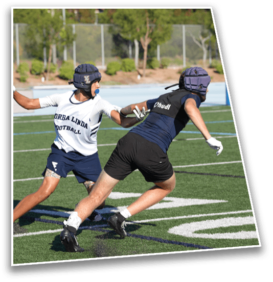 Two people wearing helmets and athletic clothing are playing football on a green field, with one person reaching out to tag the other. Description generated by AI