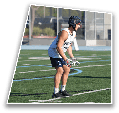 A person wearing a helmet, gloves, a sleeveless shirt, and shorts is standing in a ready position on a sports field. Description generated by AI