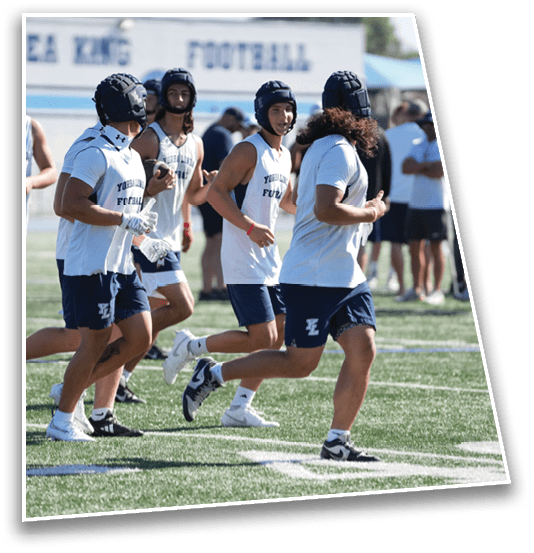 Several people wearing helmets and athletic clothing are running on a sports field during a practice or training session. Description generated by AI