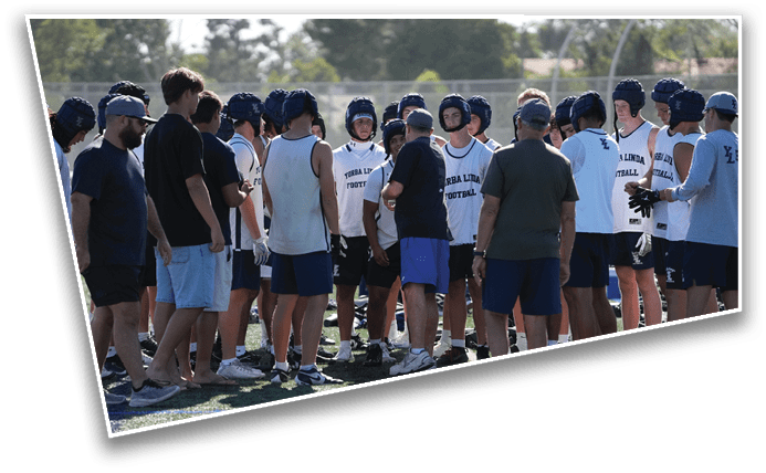 A group of people wearing sports helmets and athletic clothing are gathered on a field, seemingly preparing for or discussing a football practice or game. Description generated by AI