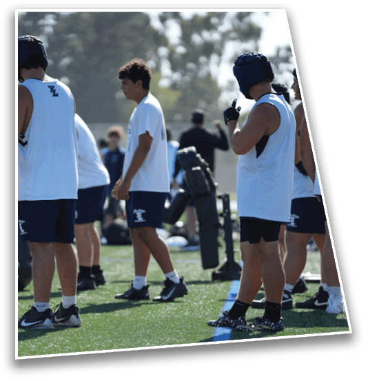 People wearing sports uniforms and helmets stand on a grassy field, appearing to prepare for or participate in an outdoor sports activity. Description generated by AI