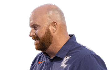 A person with a bald head and beard is wearing a navy blue collared shirt with a logo and appears to be engaged in conversation. Description generated by AI