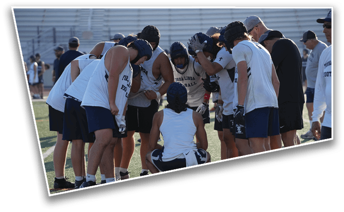 A group of people wearing sports uniforms and helmets are huddled together on a field, appearing to discuss strategy or receive instructions. Description generated by AI