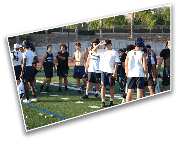 A group of people wearing athletic clothing are standing and interacting on a sports field during daylight. Description generated by AI