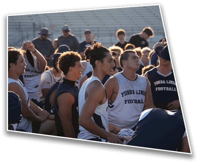 A group of people wearing sports jerseys with “Yorba Linda Football" printed on them are gathered outdoors in a stadium setting with bleachers in the background. Description generated by AI