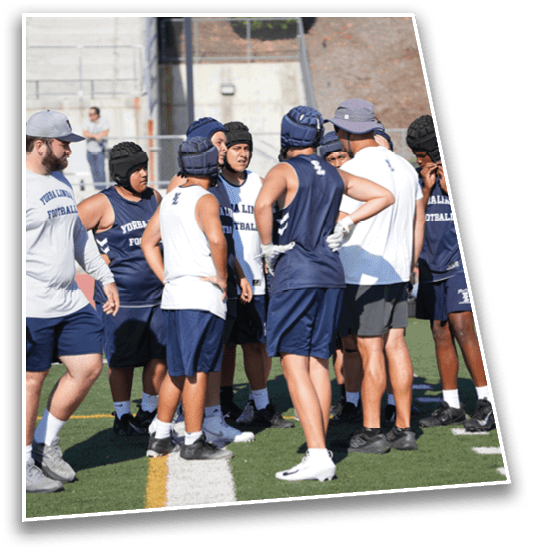 A group of people wearing athletic gear and protective headgear are gathered on a sports field, seemingly engaged in a discussion or team huddle. Description generated by AI